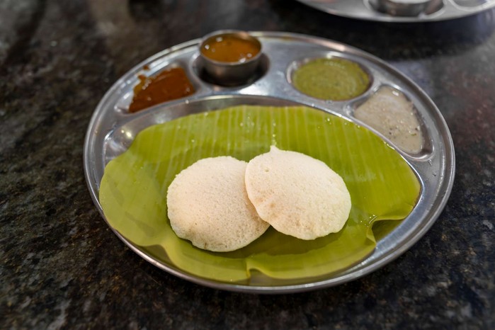 Two idlis on a leaf with dipping sauces on the side